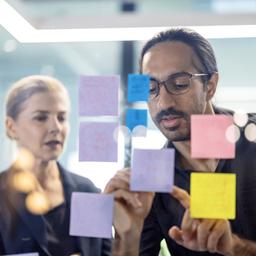 Effective project planning starts with clear visualization. Here, a junior staff member uses sticky notes to track real-time progress and align with the project owner on critical deadlines.