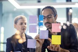 Effective project planning starts with clear visualization. Here, a junior staff member uses sticky notes to track real-time progress and align with the project owner on critical deadlines.
