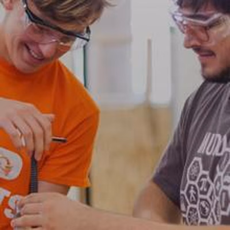 Two students wearing safety goggles and smiling as they hold a tool together