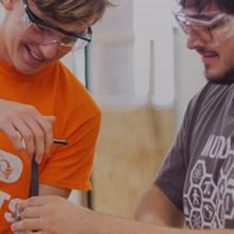 Two students wearing safety goggles and smiling as they hold a tool together
