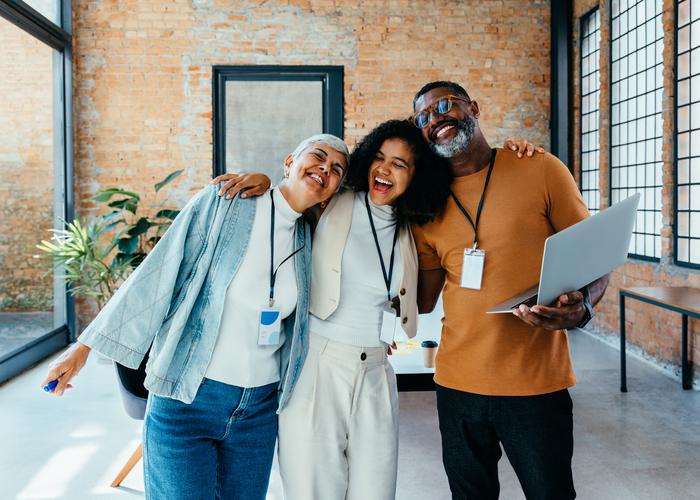 A group of diverse colleagues share a joyful moment in a modern office with brick walls and abundant natural light, representing teamwork and camaraderie.