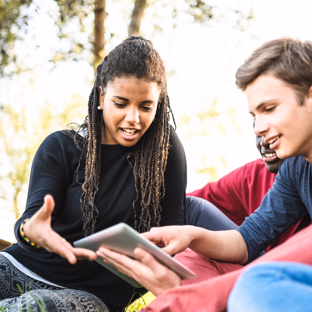 Three students sitting outside referring to a tablet computer.