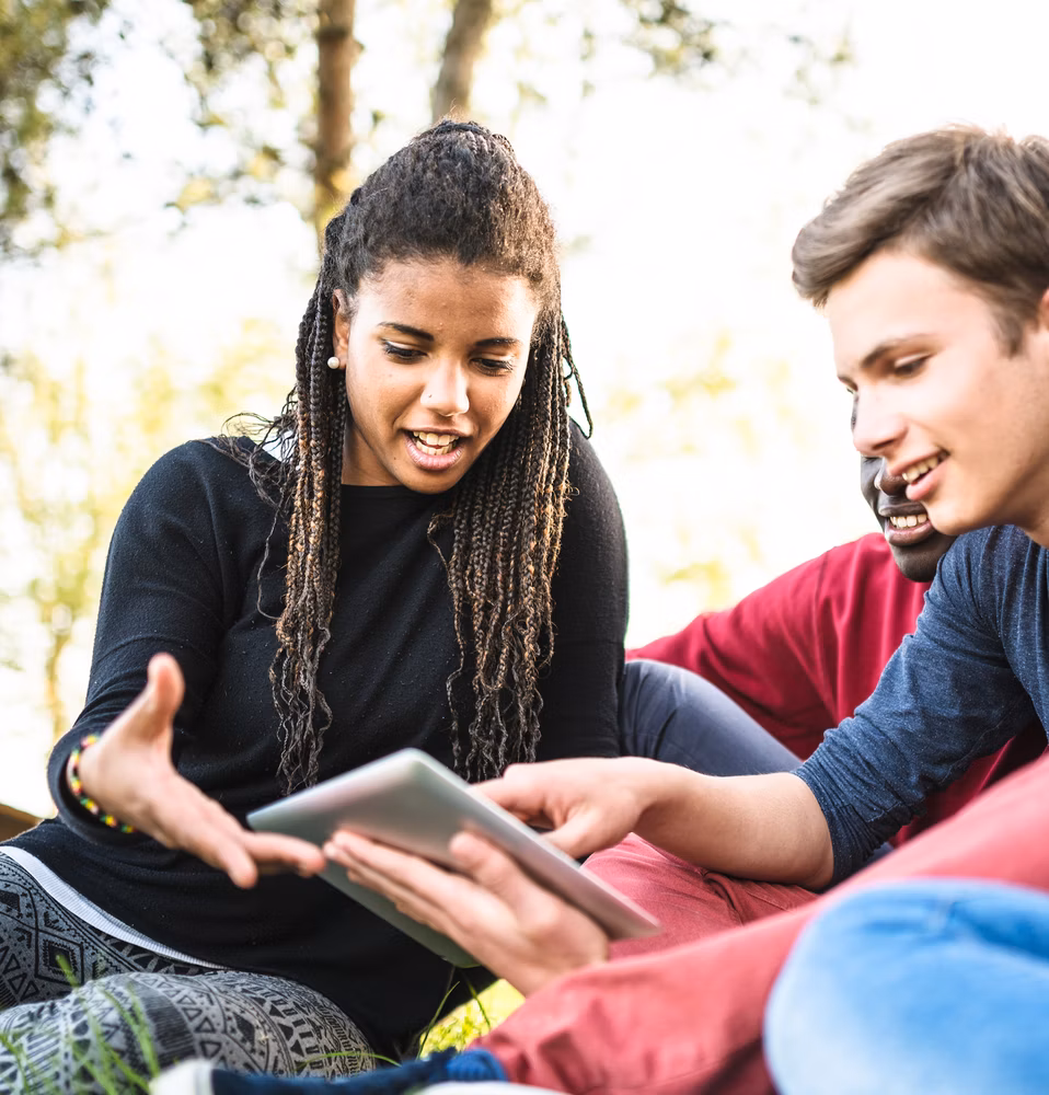 Three students sitting outside referring to a tablet computer.