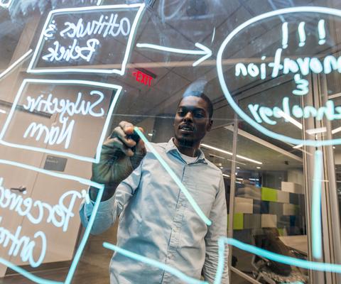 A young adult creating a flowchart with dry erase marker on a pane of glass