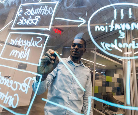 A young adult creating a flowchart with dry erase marker on a pane of glass