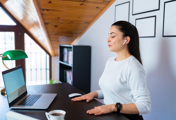 Relaxed calm business woman take deep breath of fresh air resting with eyes closed at work in home office. Doing office yoga and meditating with closed eyes.