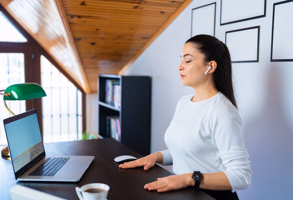 Relaxed calm business woman take deep breath of fresh air resting with eyes closed at work in home office. Doing office yoga and meditating with closed eyes.